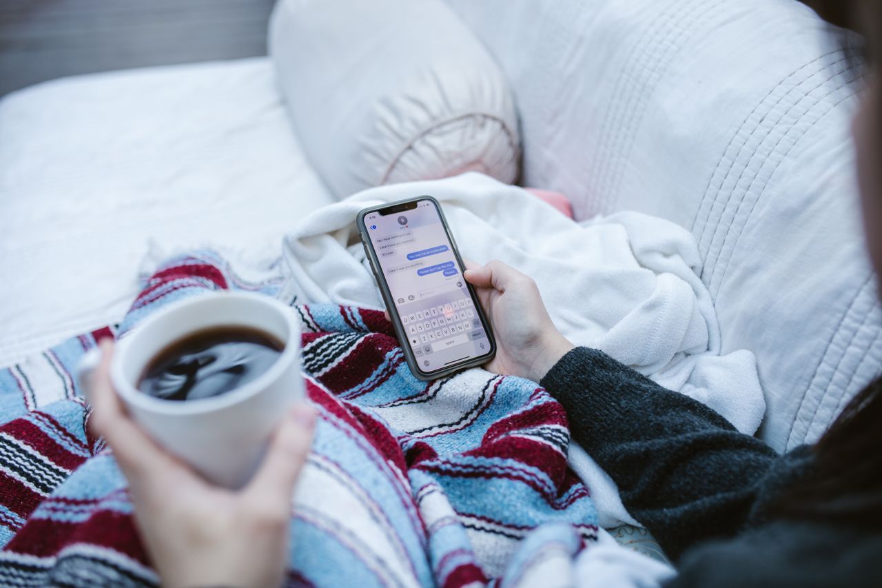 creative-02 Person relaxing indoors with coffee and smartphone, texting in a cozy setting.